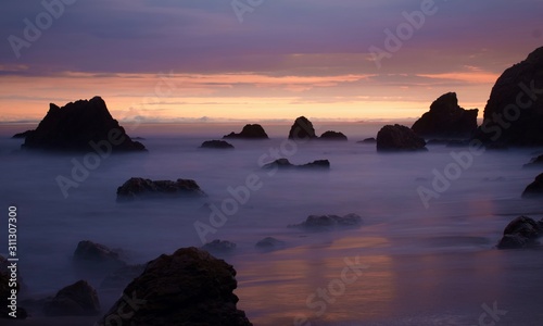 Rocks in sea, clouds against sky during sunset
