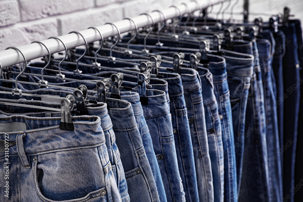 Rack with stylish jeans near brick wall, closeup Rack with stylish jeans near brick wall, closeup