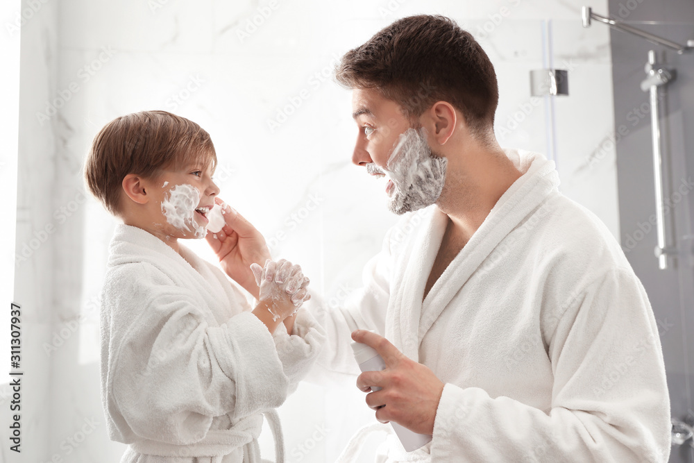 Fototapeta premium Dad applying shaving foam onto son's face in bathroom