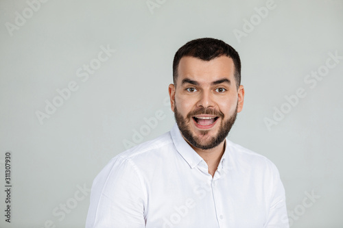 Portrait of young surprised handsome bearded man with shocked facial expression on gray background © producer