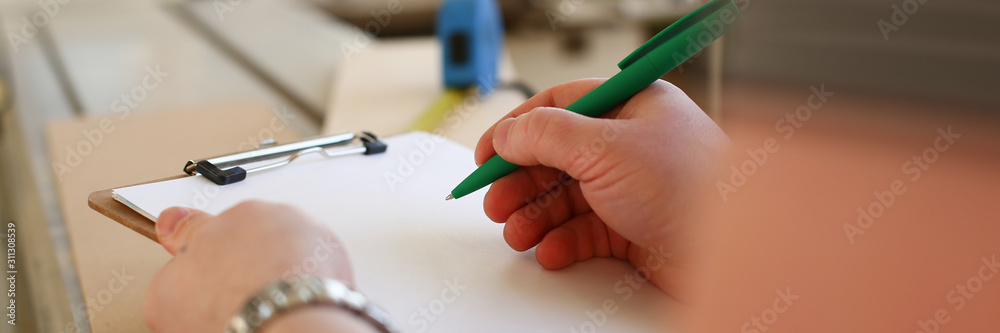 Arms of worker making notes on clipboard with green pen Arms of worker making notes on clipboard with green pen