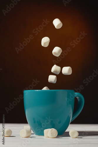Marshmallow falls into a mug of hot cocoa chocolate drink on a dark background  the concept of winter food and drink  and flying marshmallows