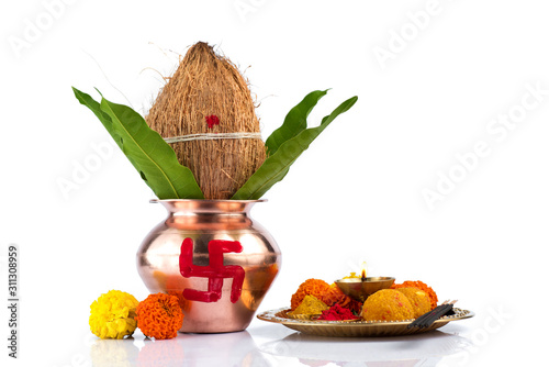 Copper Kalash with coconut and mango leaf and pooja thali with diya, kumkum and sweets with floral decoration on a white background. Essential in hindu puja.
