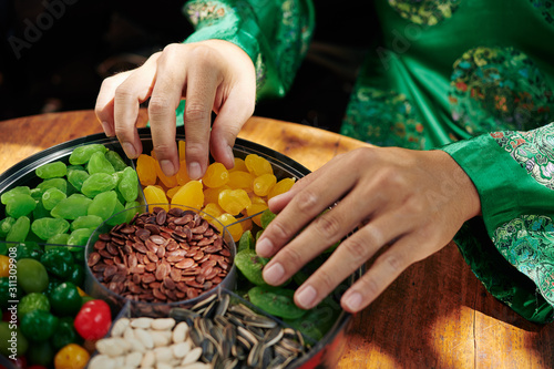 Hands of Vietnamese man in traditional costume taking dried snacks from mut plate photo