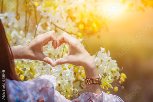 The girl raised her hand to display a meaningful heart-shaped symbol. Tell her that I love you on the blurred background of the flower garden. Showing symbols to tell love Lover on valentine's day