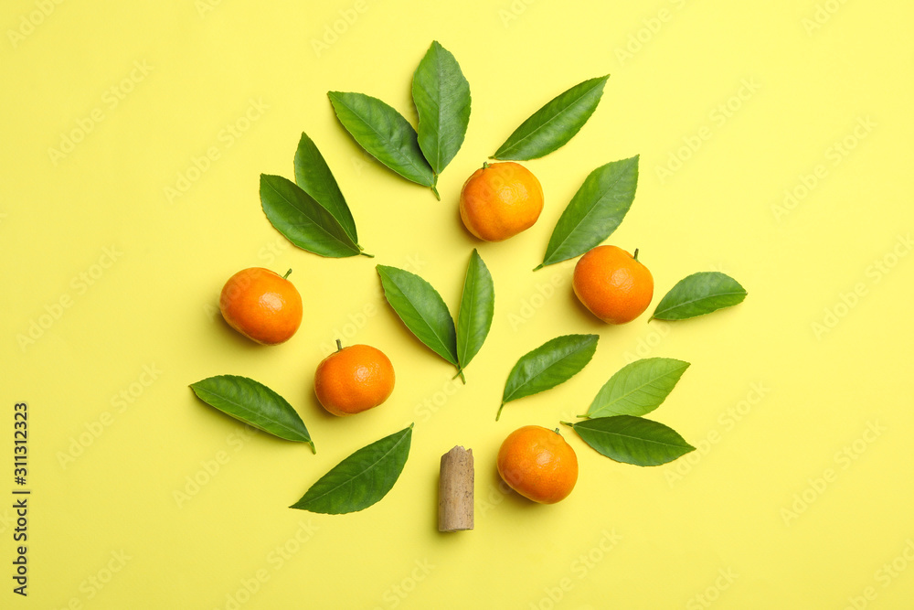 Flat lay composition with fresh green citrus leaves and tangerines on yellow background