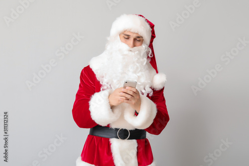 Young man in Santa costume and with mobile phone on light background