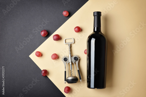 Bottle of wine, grapes and corkscrew on color background