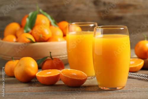 Glasses of fresh tangerine juice and fruits on wooden table