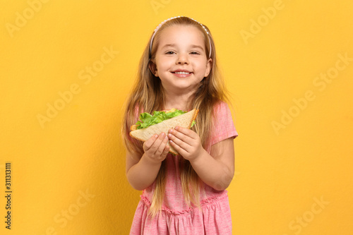 Cute little girl with tasty sandwich on yellow background