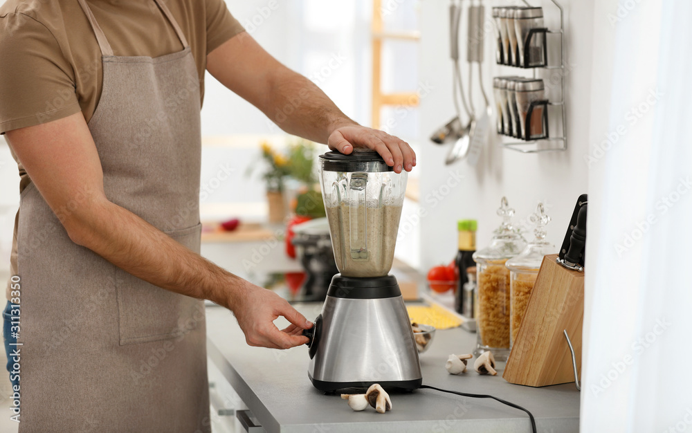 Young man using blender to cook cream soup in kitchen, closeup Young man using blender to cook cream soup in kitchen, closeup