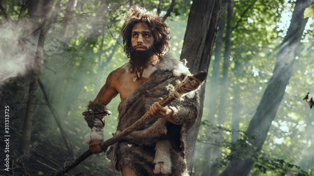 Portrait of Primeval Caveman Wearing Animal Skin and Fur Hunting with a Stone Tipped Spear in the Prehistoric Forest. Prehistoric Neanderthal Hunter Scavenging with Primitive Tools in the Jungle