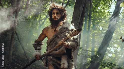 Portrait of Primeval Caveman Wearing Animal Skin and Fur Hunting with a Stone Tipped Spear in the Prehistoric Forest. Prehistoric Neanderthal Hunter Scavenging with Primitive Tools in the Jungle