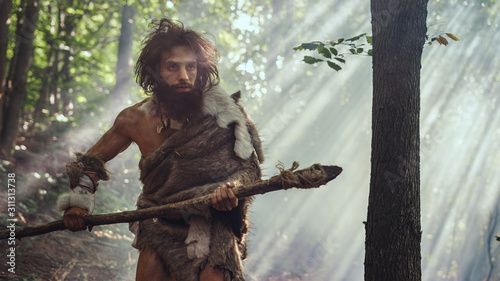 Fotografie Portrait of Primeval Caveman Wearing Animal Skin and Fur Hunting with a Stone Tipped Spear in the Prehistoric Forest