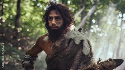 Portrait of Primeval Caveman Wearing Animal Skin and Fur Hunting with a Stone Tipped Spear in the Prehistoric Forest. Prehistoric Neanderthal Hunter Scavenging with Primitive Tools in the Jungle photo