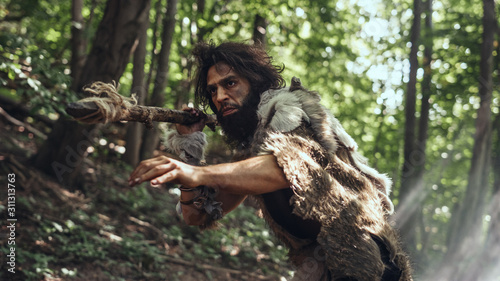 Obraz na plátně Portrait of Primeval Caveman Wearing Animal Skin and Fur Hunting with a Stone Tipped Spear in the Prehistoric Forest