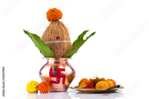 Copper Kalash with coconut and mango leaf and pooja thali with diya, kumkum and sweets with floral decoration on a white background. Essential in hindu puja.