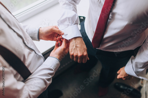 A man, a friend helps fasten the sleeves and cufflink to the groom. Hands of two men close-up. Morning and preparation of the groom. Wedding, holiday, photography.