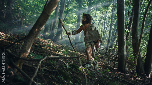 Primeval Caveman Wearing Animal Skin Holds Stone Tipped Spear Looks Around, Explores Prehistoric Forest in a Hunt for Animal Prey. Neanderthal Going Hunting in the Jungle