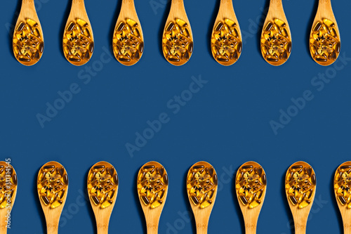 Medical classic blue background. Fish oil capsules in a wooden spoons. Flat lay, top view.
