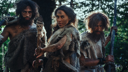 Female Leader and Two Primeval Cavemen Warriors Threat Enemy with Stone Tipped Spear, Scream, Defending Their Cave and Territory in the Prehistoric Times. Neanderthals / Homo Sapiens Tribe