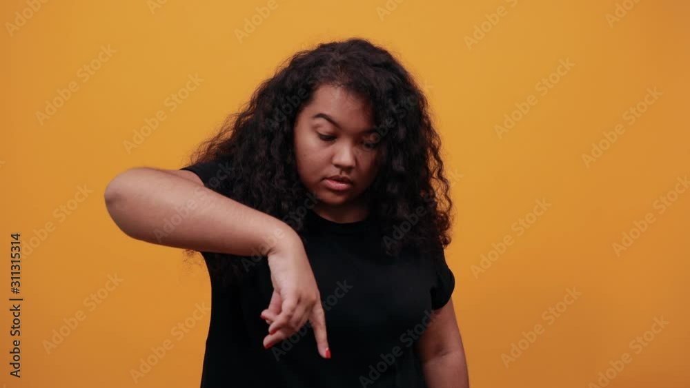 Serious afro-american young woman with overweight pointing fingers down over isolated orange background wearing fashion black shirt. People lifestyle concept. Serious afro-american young woman with overweight pointing fingers down over isolated orange background wearing fashion black shirt. People lifestyle concept.