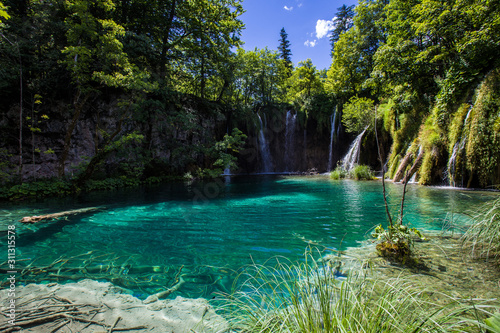 Beautiful lake landscape in the Croatian Plitvice National Park: Turquoise lake with waterfall in the background, surrounded by a dense forest and lush green vegetation © Flying broccoli