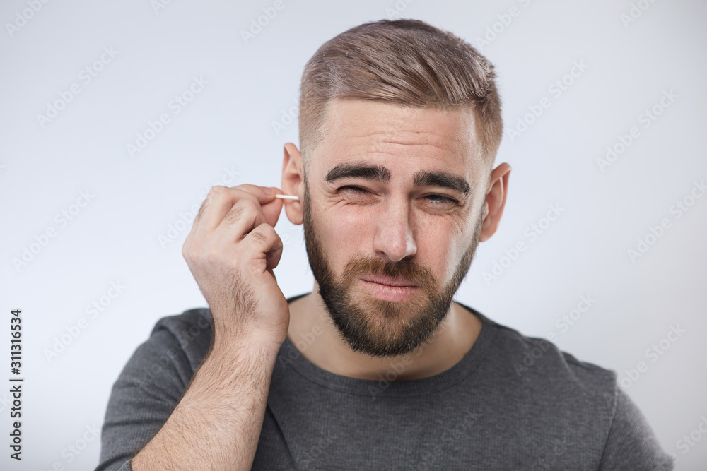Horizontal head and shoulders portrait shot of Caucasian man wearing dark gray T-shirt cleaning his ear using cotton swab, white background Horizontal head and shoulders portrait shot of Caucasian man wearing dark gray T-shirt cleaning his ear using cotton swab, white background