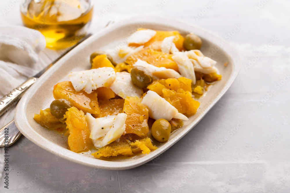 cod fish with sweet potato and olives on dish on ceramic background