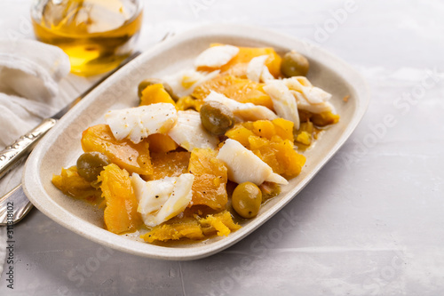 cod fish with sweet potato and olives on dish on ceramic background