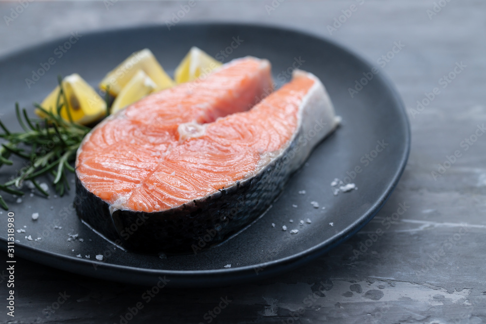 raw salmon with rosemary and lemon on dark plate raw salmon with rosemary and lemon on dark plate
