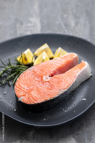 raw salmon with rosemary and lemon on dark plate