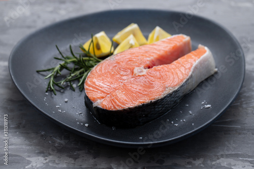 raw salmon with rosemary and lemon on dark plate