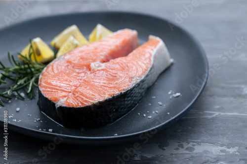 raw salmon with rosemary and lemon on dark plate