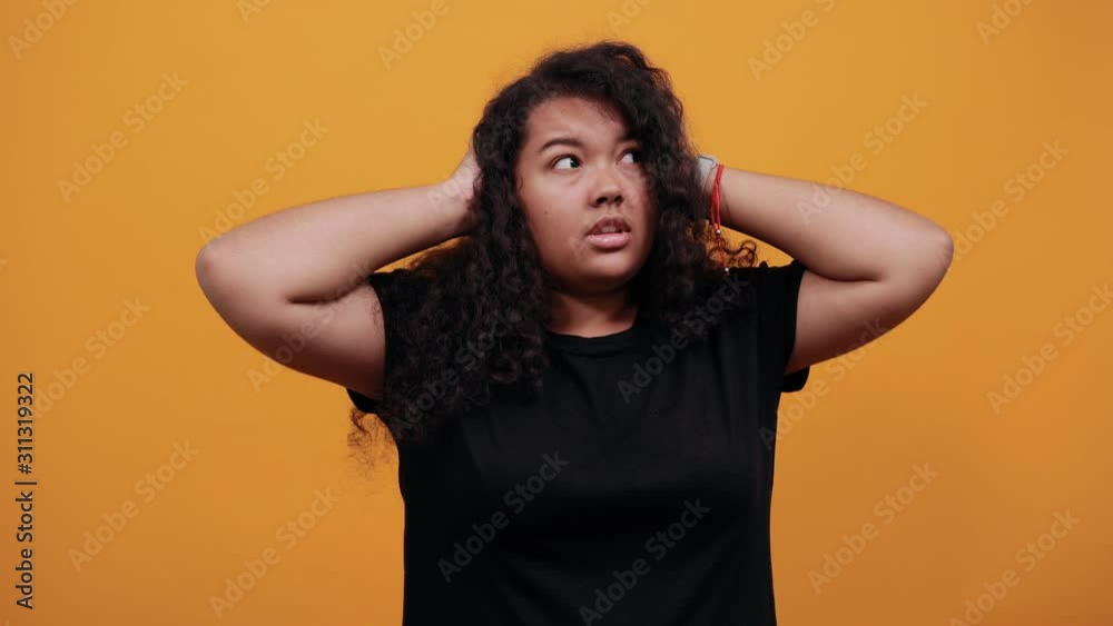 Shocked afro-american young woman with overweight over isolated orange background wearing fashion black shirt keeping hands on head, corrects haircut. People lifestyle concept.