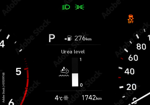 Close up of urea level indicator on car dashboard panel located between speedometer and tachometer. Car instrument panel with traction control warning light, low beam and side light indicators.