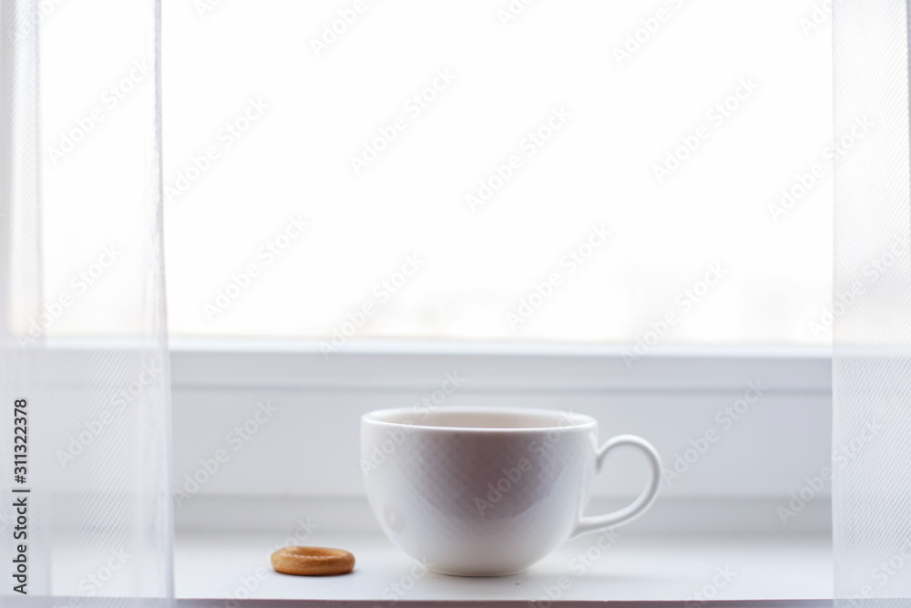 white cup with tea stands on the windowsill on the window
