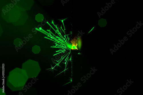 Sparkler in green and white light on a black background