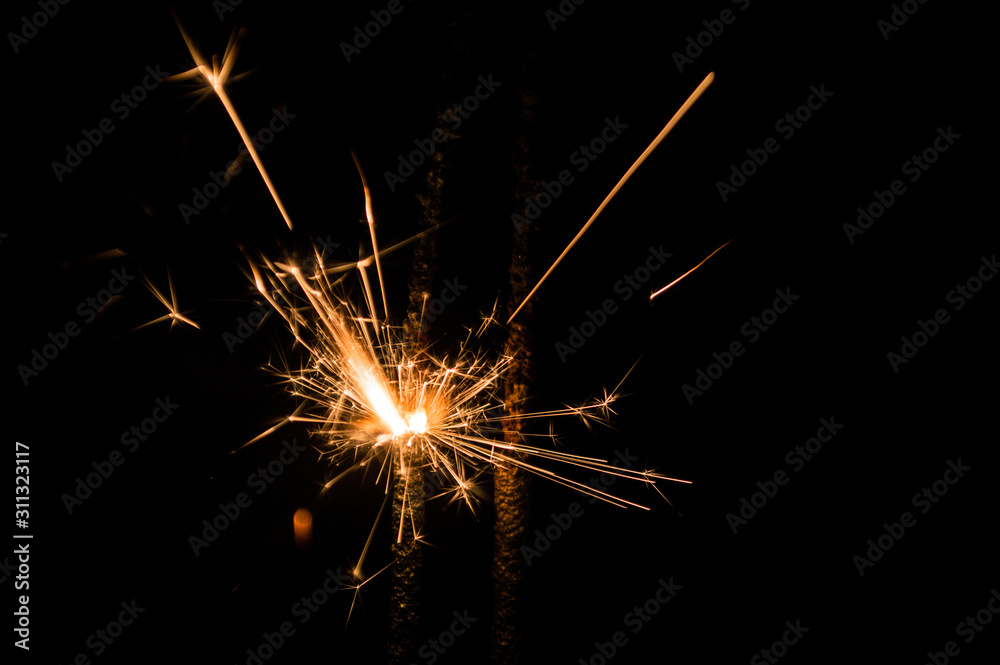Sparkler in yellow and orange light on a black background.