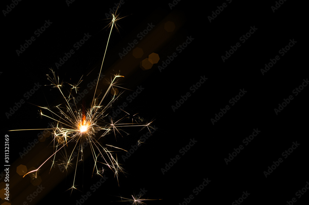 Obraz premium Sparkler in yellow and orange light on a black background.