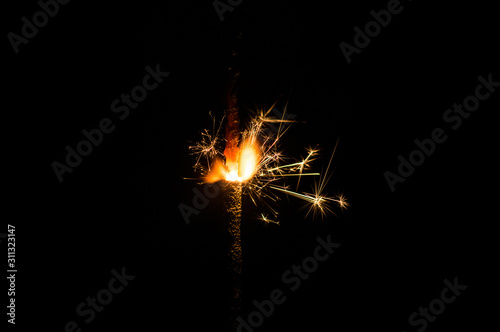 Sparkler in yellow and orange light on a black background.