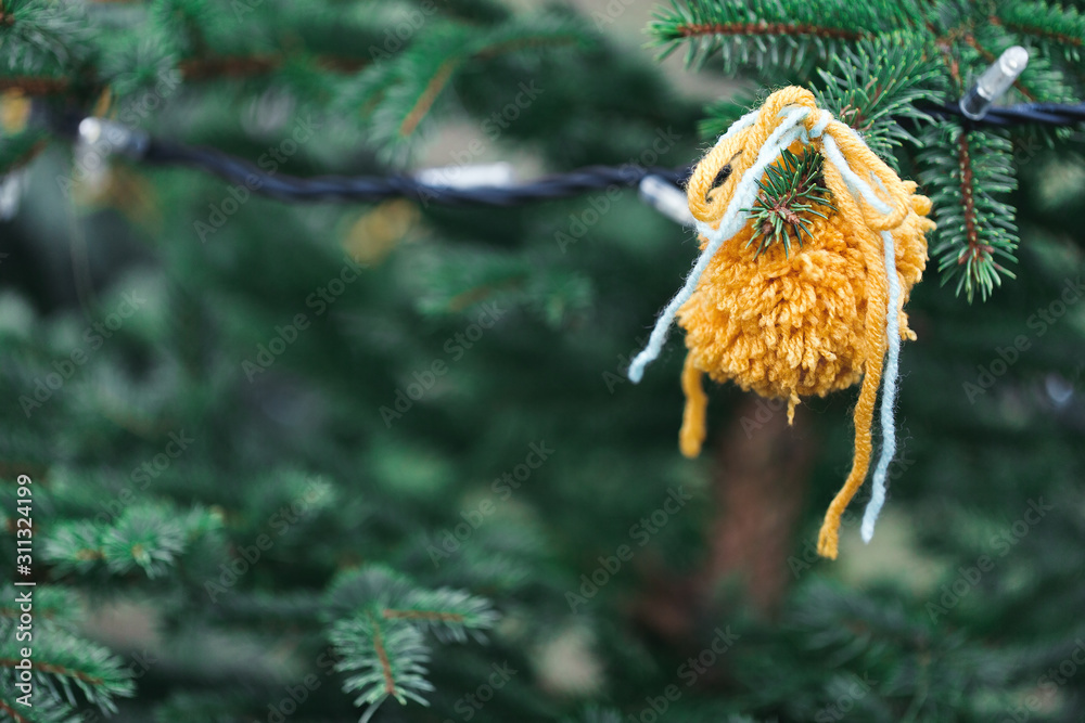 Fototapeta premium Wool handmade decoration on a Christmas tree outdoor. Diy yarn crafts creative ideas for children. Environment, recycle and zero waste concept. Selective focus, copy space.