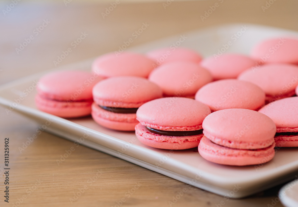 Beautiful pink macaroons with chocolate ganache on a white square plate stand on a wooden table Beautiful pink macaroons with chocolate ganache on a white square plate stand on a wooden table