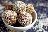Raw food balls.Handmade vegan sweets made from almonds, walnuts, dates, raisins, coconut and cocoa. Raw food candies in coconut and cocoa close-up on white paper on a dark table laid out in rows. 