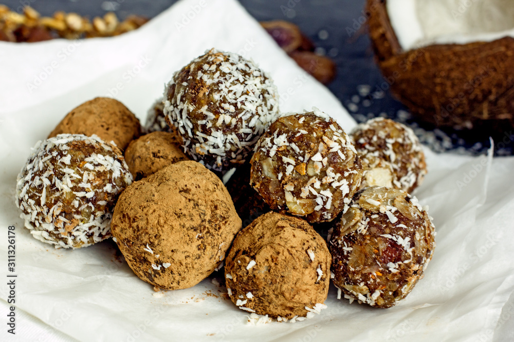 Raw food balls.Handmade vegan sweets made from almonds, walnuts, dates, raisins, coconut and cocoa. Raw food candies in coconut and cocoa close-up on white paper on a dark table laid out in rows. Raw food balls.Handmade vegan sweets made from almonds, walnuts, dates, raisins, coconut and cocoa. Raw food candies in coconut and cocoa close-up on white paper on a dark table laid out in rows.