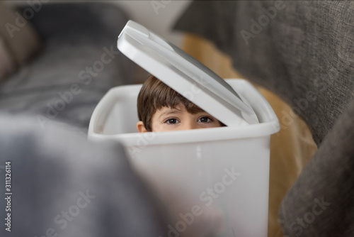 Hidden boy in dirty clothes basket looking at camera
