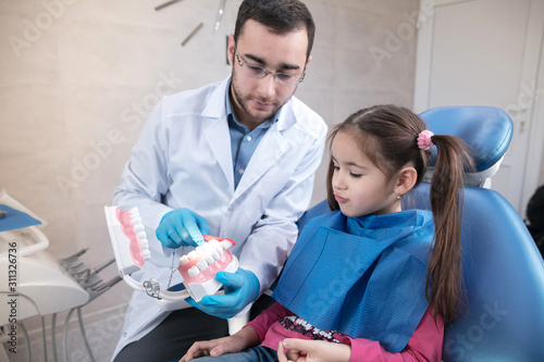 Young caucasian girl exploring teeth structure visiting dentist's office for prevention of the oral cavity. Child and doctor while checkup teeth. Healthy lifestyle, healthcare and medicine concept.