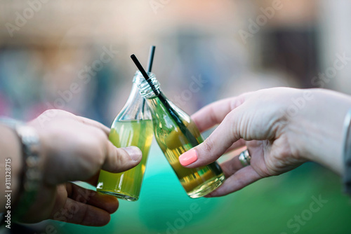 Small mini bottles with a green drink and straws in their hands. Street food.