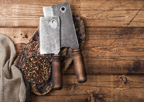 Vintage hatchets for meat on wooden chopping board with salt and pepper on wooden table background with linen towel.