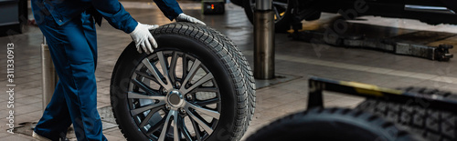 cropped view of mechanic with car wheel in workshop, panoramic shot
